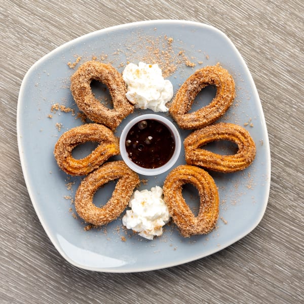 Six churros dusted with cinnamon sugar, whipped cream, and chocolate dipping sauce on a blue plate.