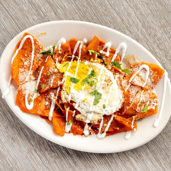 Chilaquiles with red sauce, a fried egg, sour cream, cheese, and cilantro on a white plate.