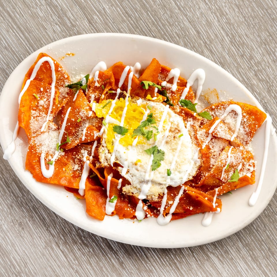 Chilaquiles with red sauce, a fried egg, sour cream, cheese, and cilantro on a white plate.