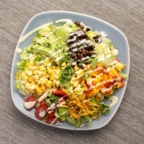 Taco salad with avocado, black beans, corn, bell peppers, tomatoes, and tortilla strips.