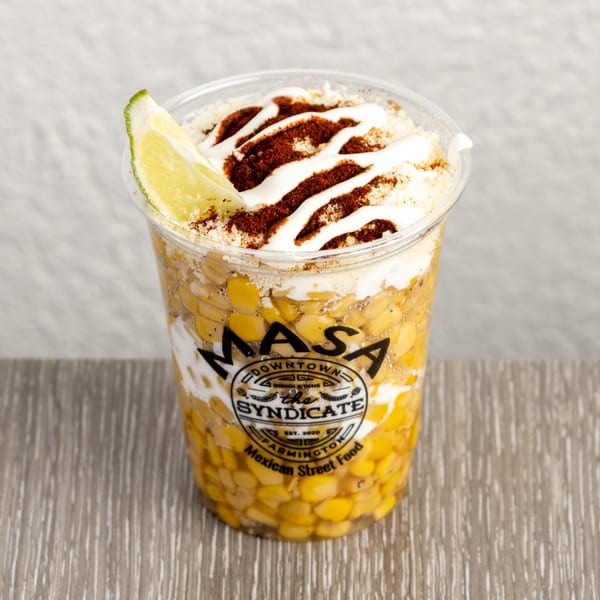 Masa Syndicate Mexican Street Food elote in a cup with lime, crema, and chili powder.