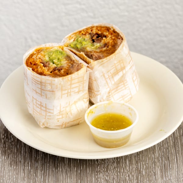 Two burritos, cut in half, revealing rice, beans, and guacamole, with a side of green salsa.