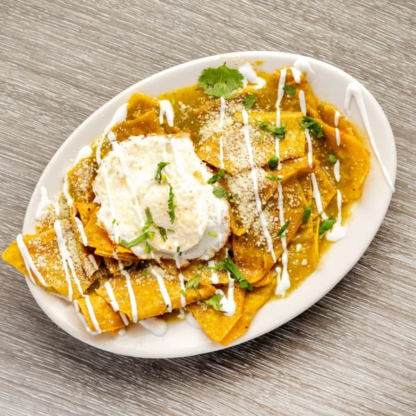 Chilaquiles with green sauce, sour cream, cheese, and cilantro on a white oval plate.